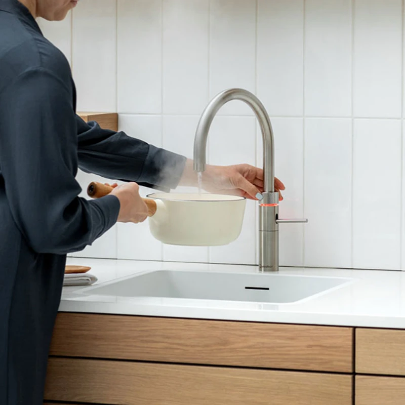 Frau füllt mit einem Quooker Fusion Round in Edelstahl einen Topf mit kochendem Wasser